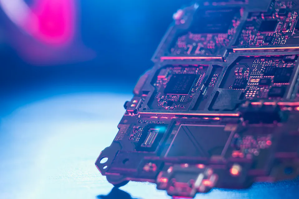 Semiconductor Industry Eine Nahaufnahme einer Computerplatine, die mit leuchtenden blauen und pinken Lichtern beleuchtet wird, zeigt komplexe Schaltkreise und elektronische Komponenten in einem technologischen und futuristischen Ambiente.