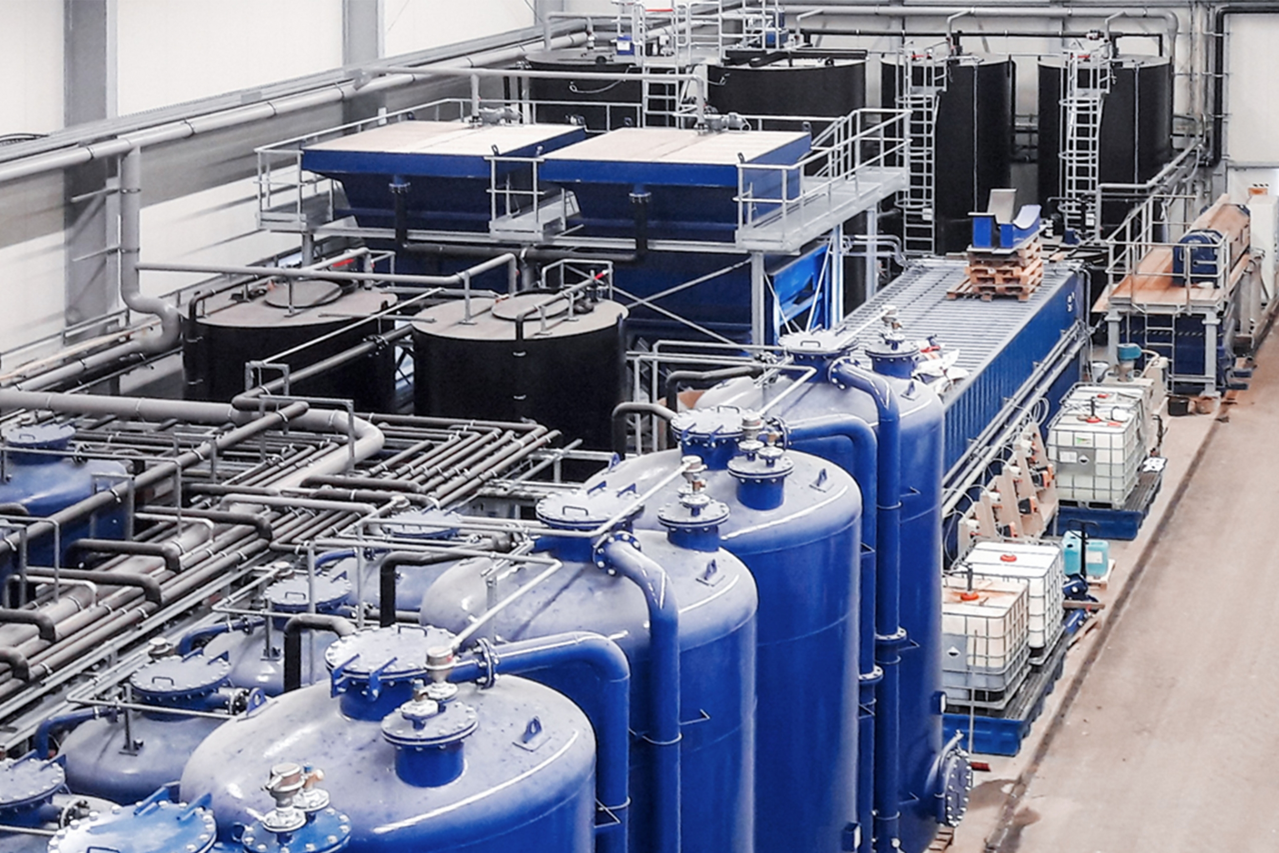 Eine moderne Wasseraufbereitungsanlage mit blauen Tanks und komplexen Rohrleitungen, eingebettet in einem industriellen Umfeld.