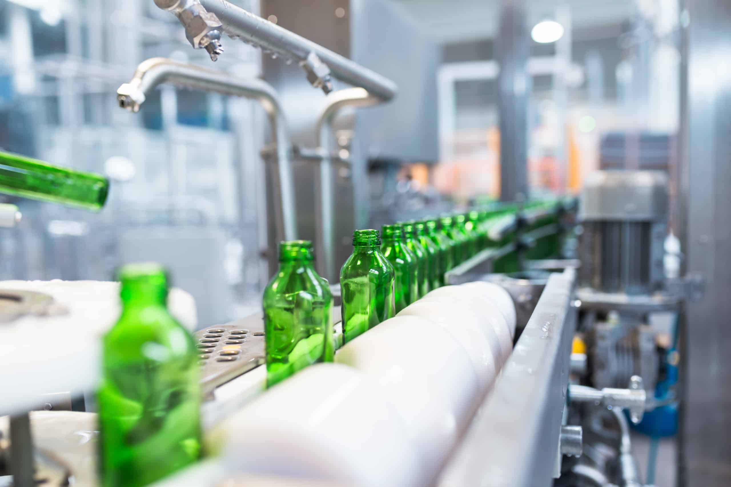 A row of green glass bottles moves along an automated conveyor belt in a modern bottling facility, emphasizing industrial automation and efficiency.