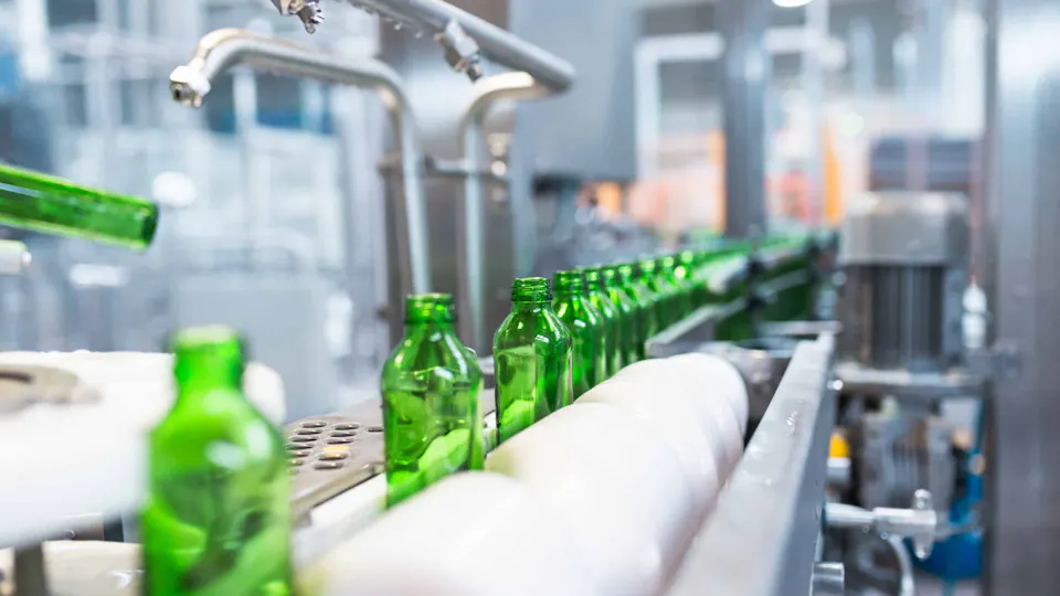 Water manufactur A row of green glass bottles moves along an automated conveyor belt in a modern bottling facility, emphasizing industrial automation and efficiency.