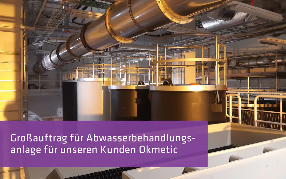 Großauftrag: Okmetic Eine industrielle Abwasserbehandlungsanlage mit mehreren großen Tanks und Rohrleitungen, umgeben von einem komplexen Netz aus Metallstrukturen, alles in einem gut beleuchteten, modernen Fabrikgebäude.