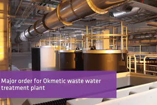 Major order for Okmetic A modern industrial interior of a wastewater treatment plant is shown, featuring large cylindrical tanks and extensive overhead piping, with warm lighting illuminating the metallic surfaces.