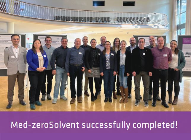 Group photo of women and men in a large hall with display boards in the background, wooden floor and gallery.