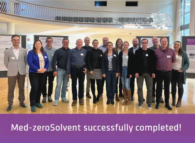 Med-ZeroSolvent Completed Group photo of women and men in a large hall with display boards in the background, wooden floor and gallery.