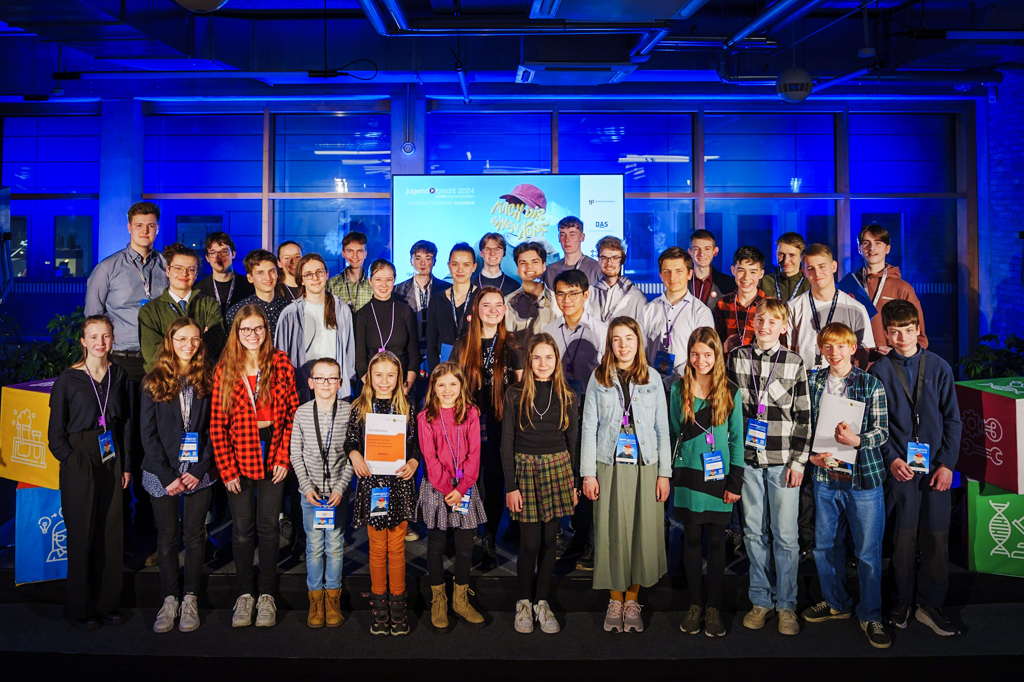 The group photo shows a diverse group of young participants in “Youth Research,” all smiling in a modern event room.