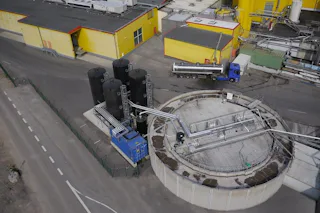 Friweika Germany An aerial view of an industrial facility featuring large storage tanks and a cylindrical structure with interconnected pipelines, a blue truck is parked nearby for maintenance, highlighting industrial operations and logistics.
