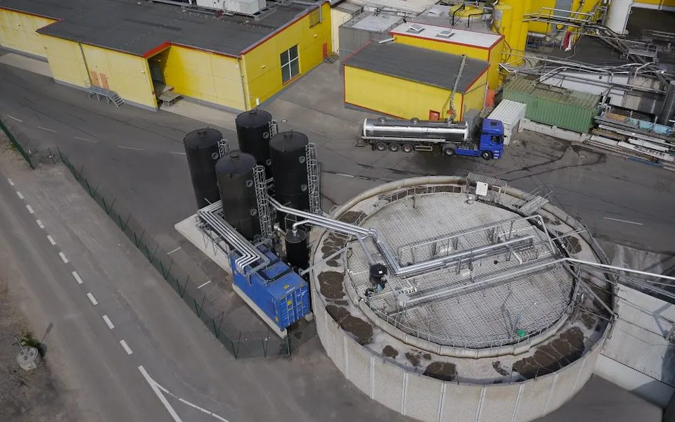 Friweika Germany An aerial view of an industrial facility featuring large storage tanks and a cylindrical structure with interconnected pipelines, a blue truck is parked nearby for maintenance, highlighting industrial operations and logistics.