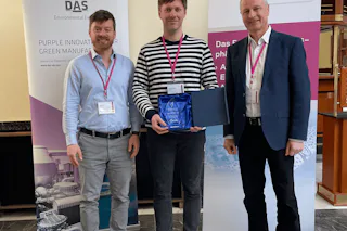 enaDyne Personen stehen lächelnd in einem Bürogebäude vor zwei Roll-Up-Bannern, während eine Person eine blaue Auszeichnung hält.