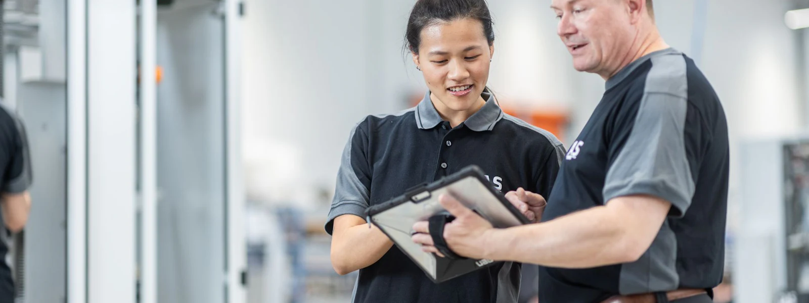 Production workers In a modern factory environment, two people in work clothes discuss a tablet, surrounded by industrial machinery and production equipment.