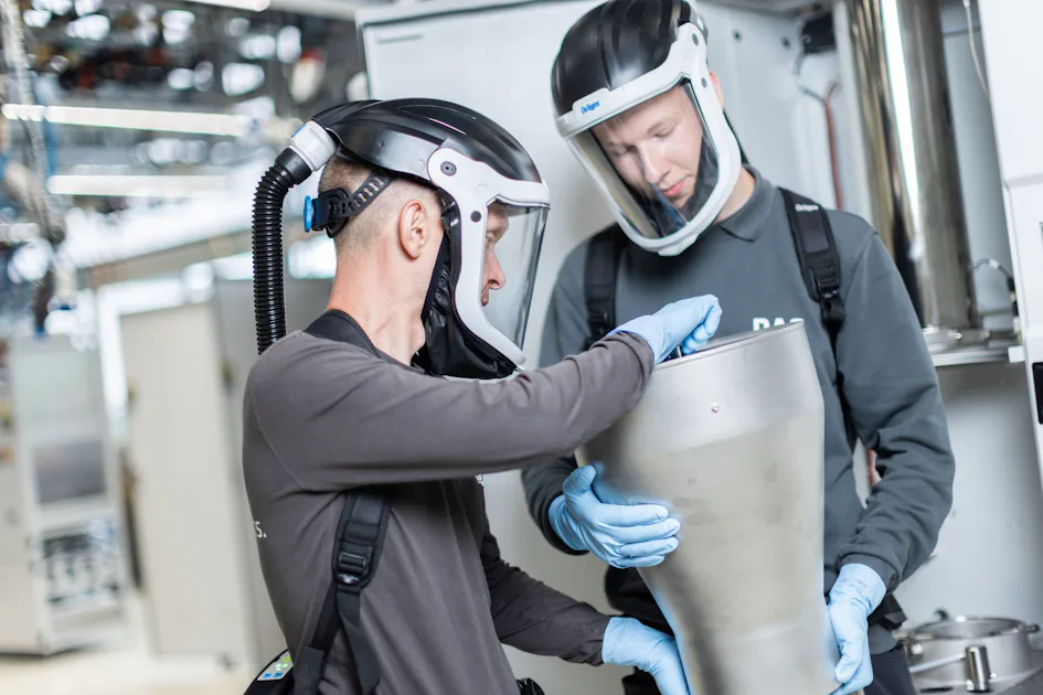Waste Gas Treatment Two individuals wearing protective face shields and gloves work collaboratively with industrial equipment in a modern facility, focusing on handling a large metallic component.
