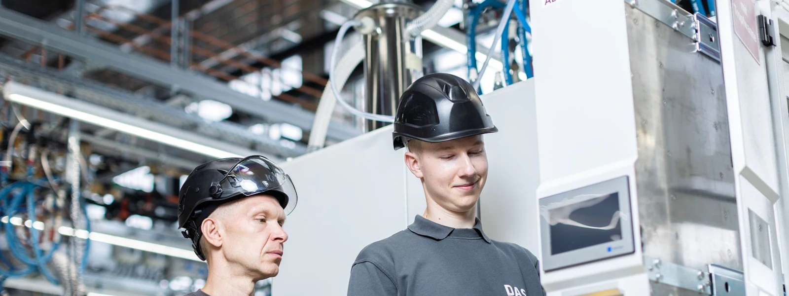 DAS service engineers at the switch cabinet Two workers wearing safety helmets operate a modern industrial control console in a factory environment.