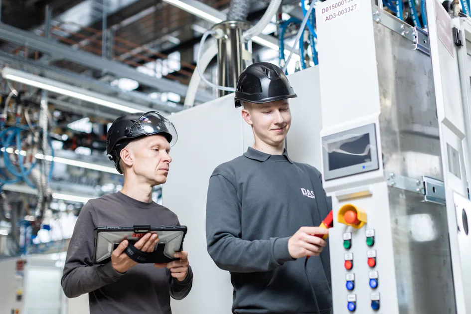 DAS service engineers at the switch cabinet Two workers wearing safety helmets operate a modern industrial control console in a factory environment.
