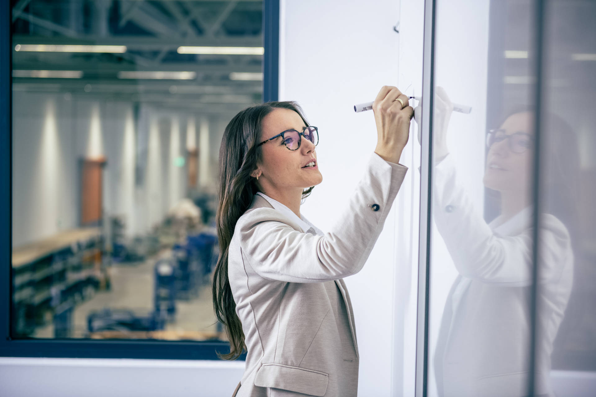 A professional executive in a modern working environment writes on a whiteboard, strategizing for process optimization and project management while focusing on office and production innovation.