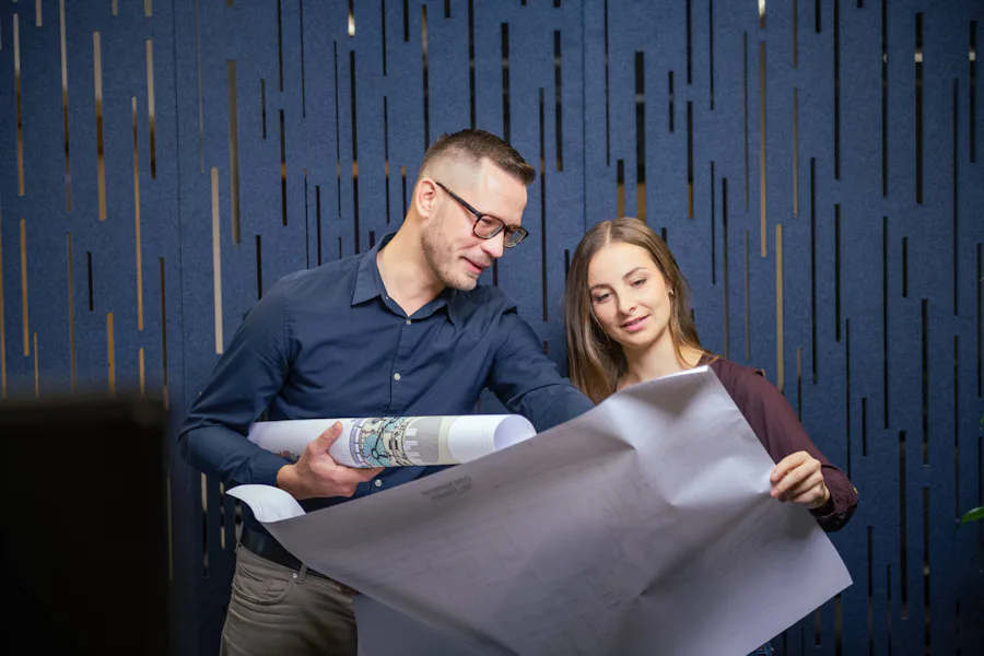 DAS Employees Water Treatment 1 Zwei Personen betrachten gemeinsam Baupläne und Architekturzeichnungen vor einem modernen, blau gestreiften Hintergrund.
