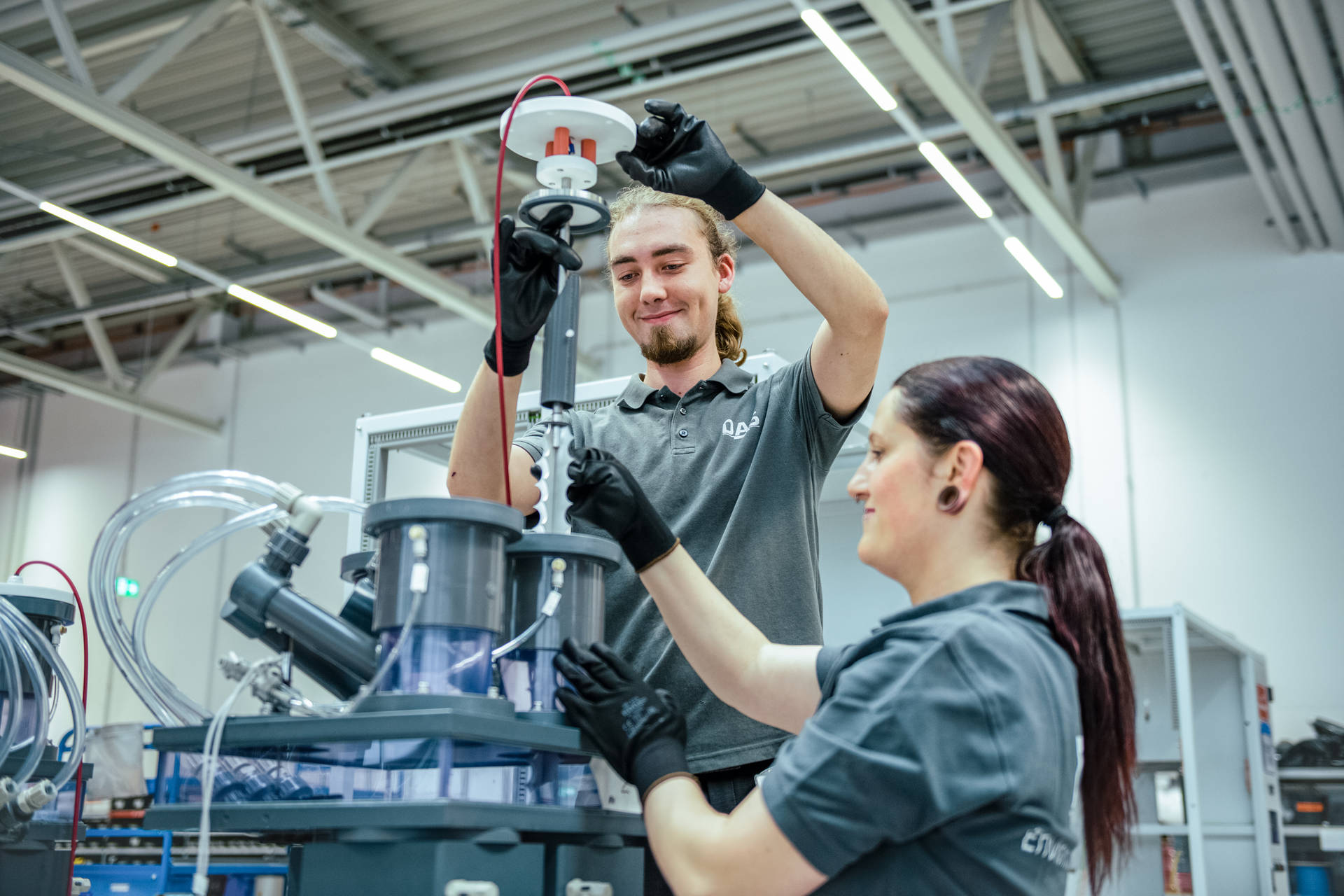 Two assembly workers in a factory are installing components into a complex machinery system, highlighting teamwork in production and assembly technology.