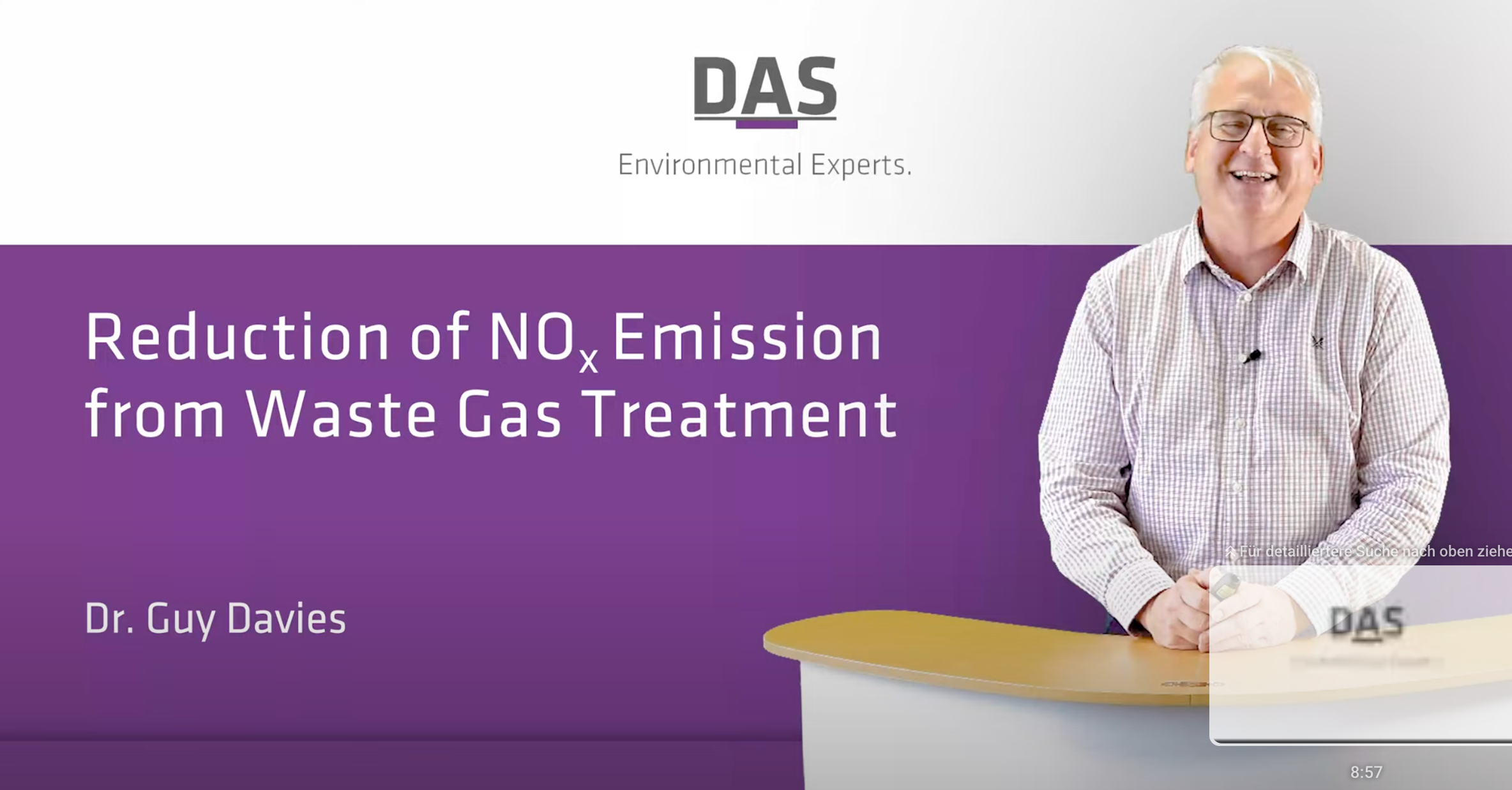 A smiling individual stands beside a curved desk with a purple and white backdrop displaying the text "Reduction of NOx Emission from Waste Gas Treatment" and "Dr. Guy Davies," under the "DAS Environmental Experts" logo.