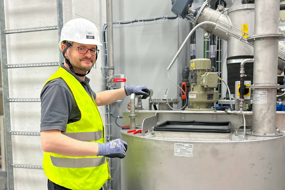 Cold Commissioning at Okmetic A worker wearing a white hard hat and a yellow safety vest operates machinery in an industrial setting, surrounded by metal pipes and control equipment.