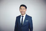 Bin Wu, General Manager A person in a blue suit and tie smiles confidently against a plain white background, capturing a professional and approachable demeanor.