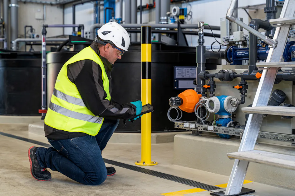 Maintenance of Wastewater Treatment Systems by DAS experts A worker in a safety vest and hard hat kneels beside an array of industrial machinery in an industrial plant, inspecting equipment and taking notes, emphasizing maintenance in a high-tech environment.