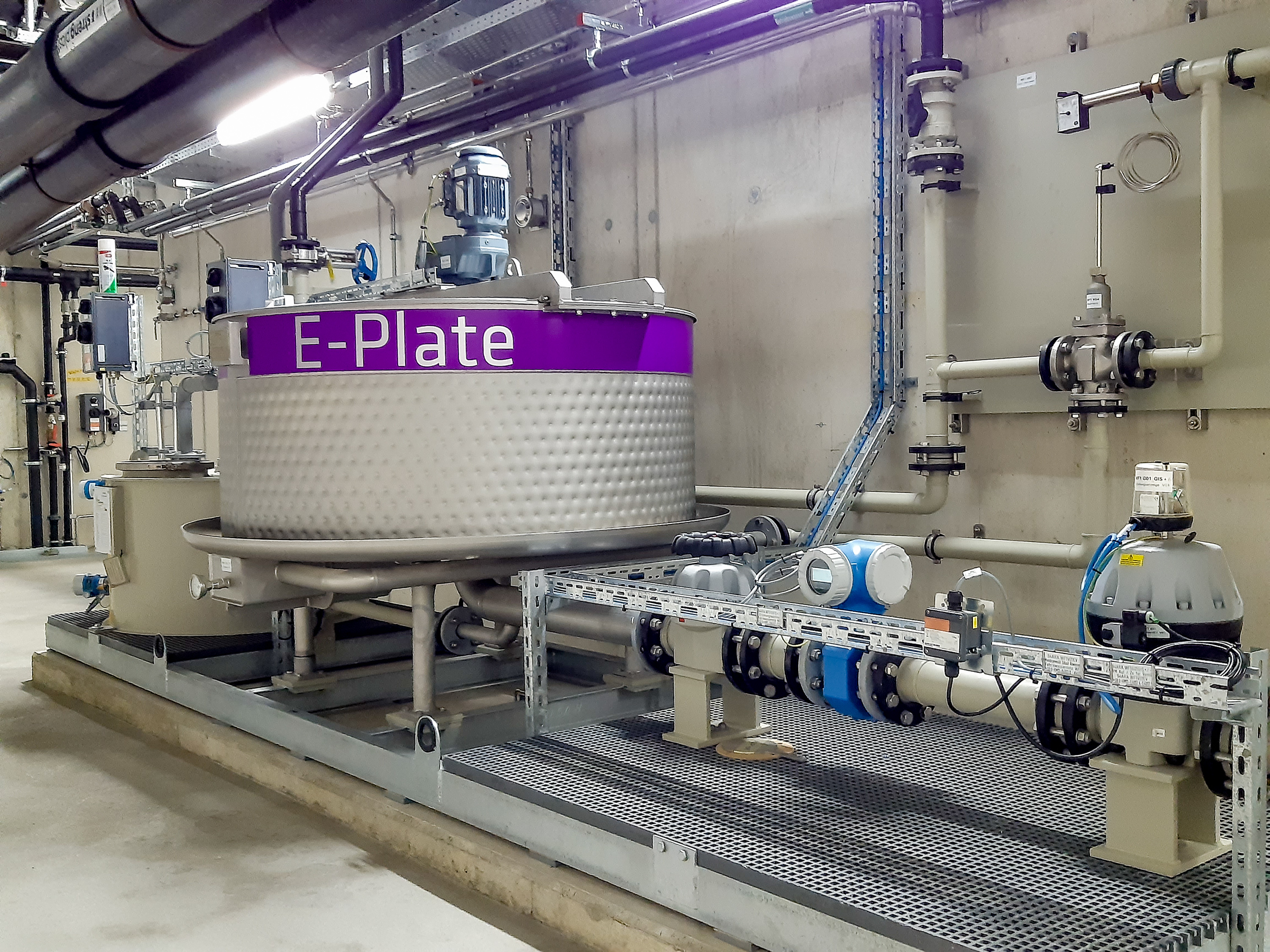 An industrial heat exchanger labelled ‘E-Plate’ stands in a modern plant room, surrounded by pipes and valves, manufactured by DAS Environmental Experts.