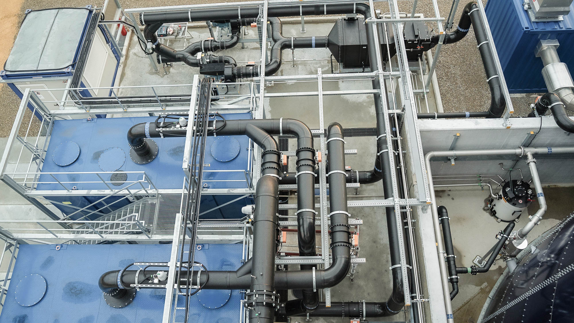 Industrieanlage mit verzweigten Rohrleitungen, mehreren blauen Tanks und einem komplexen Netz von metallischen Strukturen in einer Außenumgebung.
