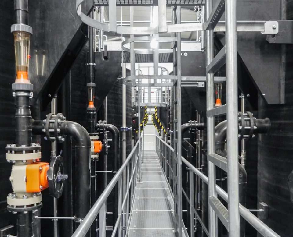 Kesslergrube Cover An industrial plant room with multiple pipes and valves flanks a metal maintenance walkway that runs through a modern factory environment.