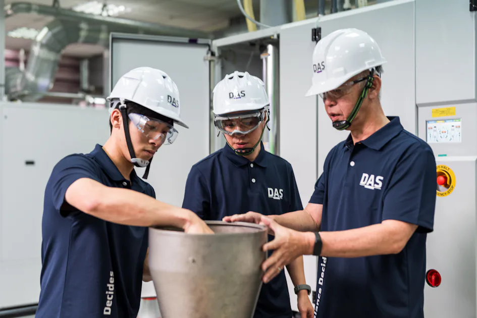 說明 三位穿著藍色工作服並佩戴白色安全帽和護目鏡的工人正專注地在工廠內檢查一個大型金屬容器。