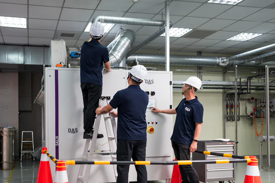 機台檢測-1 三位戴著安全帽的人員在明亮的工業設施中,操作大型金屬設備,專注於機器的檢查和維護,周圍有橙白相間的安全欄杆。