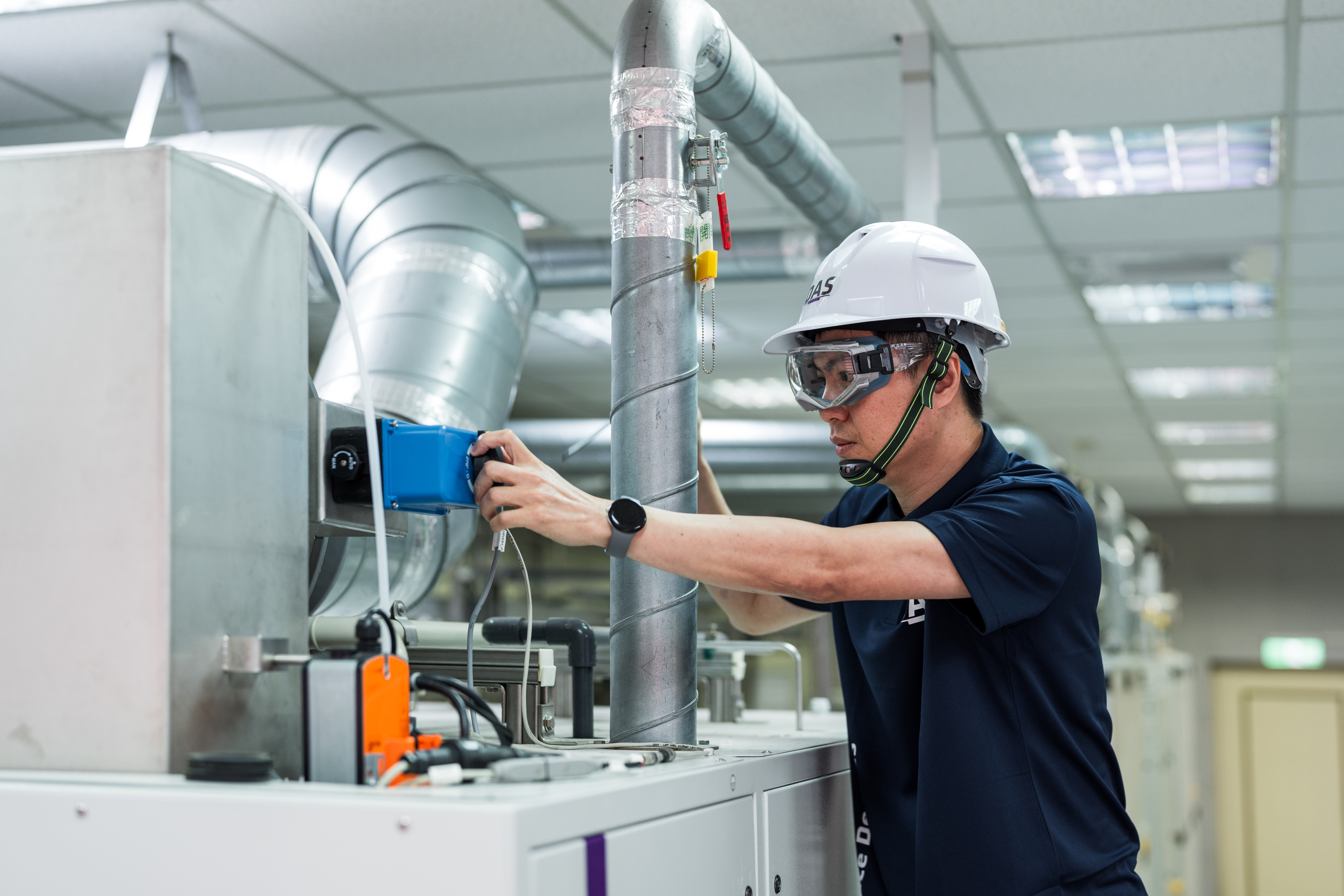 一名穿著安全帽和護目鏡的技術員正在檢查通風系統，背景是工業環境，顯示現代化設備與管道設置。