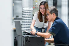 討論公事 一名年輕女子與一名中年男子在現代辦公環境中一起專注於筆記型電腦上的工作。