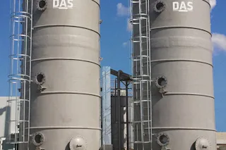 Wastewater Treatment Cheese Production The image shows two large industrial grey storage tanks labeled with "DAS," standing side by side under a clear blue sky, connected by a network of metallic pipes and surrounded by a grassy area.