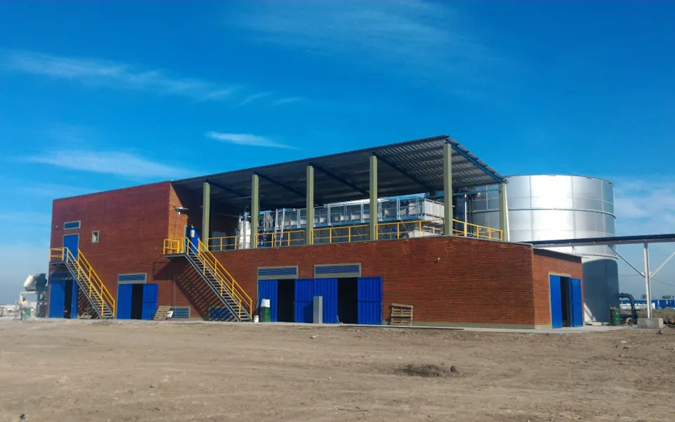 Exterior view of REFRES NOW S.A. Building of a beverage manufacturer with red brick, blue doors and windows, and a silver water tank in the background under a clear blue sky.