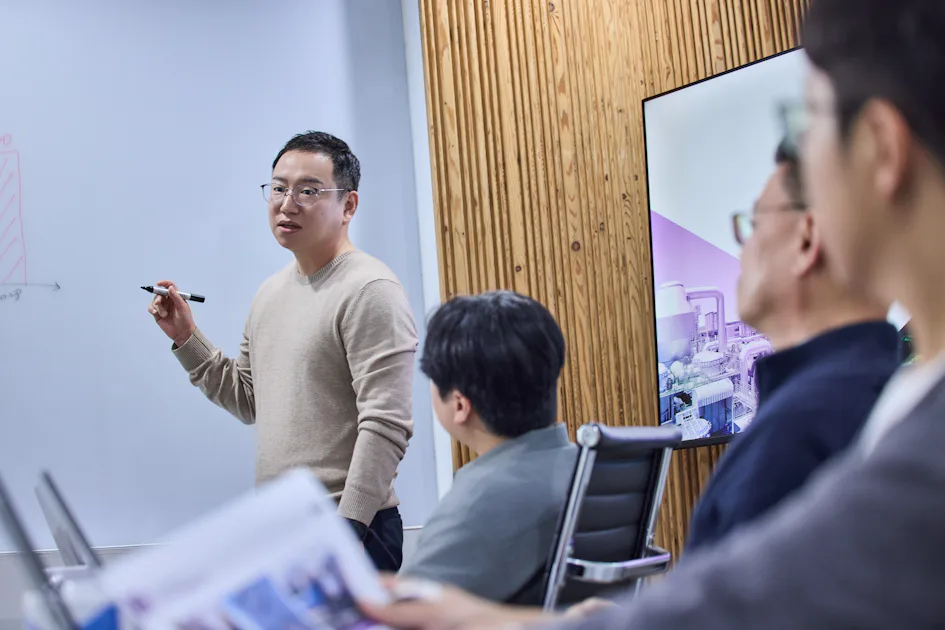 논의 4 명의 직원이 현대적인 사무실의 회의 테이블에 둘러앉아 이야기를 나누고 있다. 가운데 있는 사람은 노트북을 들고 집중하고 있는 모습이다.