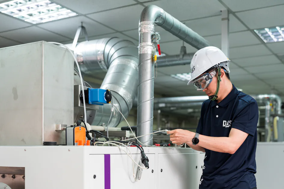 機台檢測 工廠中穿著工作服與安全帽的技術員正在檢查機械設備,周圍可見複雜的管道和儀表板,專注於機械保養工作。