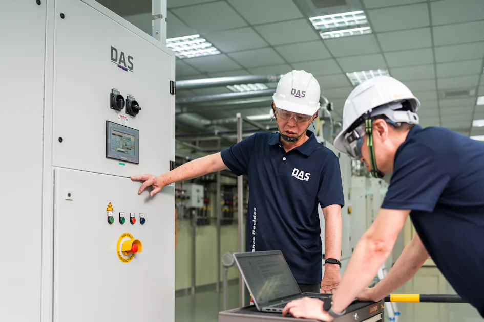 規劃與討論 兩位身穿制服和安全帽的工程師在現代化工廠內檢查工業控制面板,一位正查看控制裝置,另一位在筆記型電腦上記錄數據。