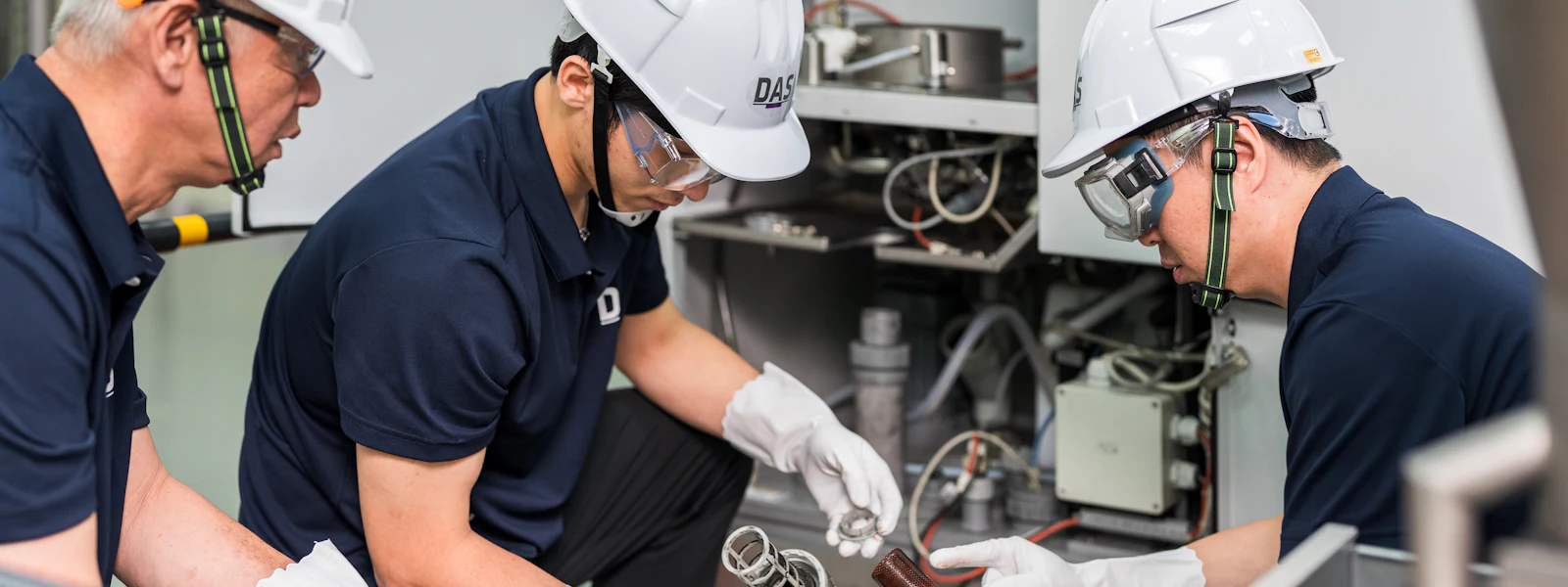 機台測試 三位戴著白色安全帽的技術人員正在檢查工業設備的運行情況,設備周圍有複雜的管線和控制面板,強調安全和精確的工業維護。
