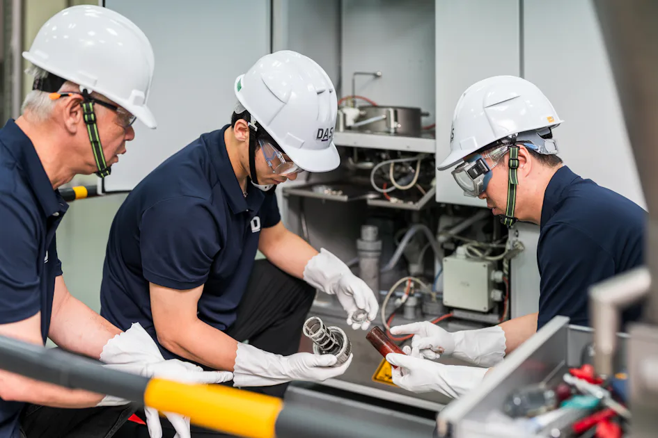 機台測試 三位戴著白色安全帽的技術人員正在檢查工業設備的運行情況,設備周圍有複雜的管線和控制面板,強調安全和精確的工業維護。