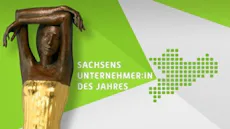 Sachsen Unternehmer:in des Jahres 這幅圖像展示了一座雕塑,雕塑的上半部呈現出一位人物雙臂高舉的姿勢,背景是綠色和白色的幾何圖案,左側有「SACHSENS UNTERNEHMER:IN DES JAHRES」的文字。
