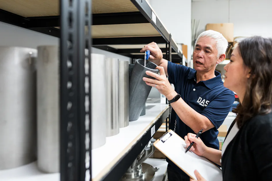 Parts 測量 兩位工作人員在倉庫中檢查一個大型金屬零件,其中一人手持計量工具,另一人正在筆記本上記錄數據。