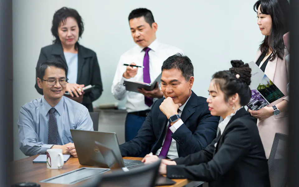 案例分享 一群商務人士在會議室中專注於筆記型電腦屏幕,進行團隊合作和交流,幾位成員正忙於記錄和討論。