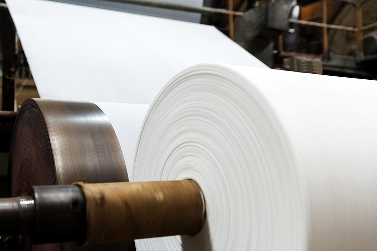 A large roll of white paper is being processed on an industrial printing machine, highlighting the manufacturing process in a commercial print shop.
