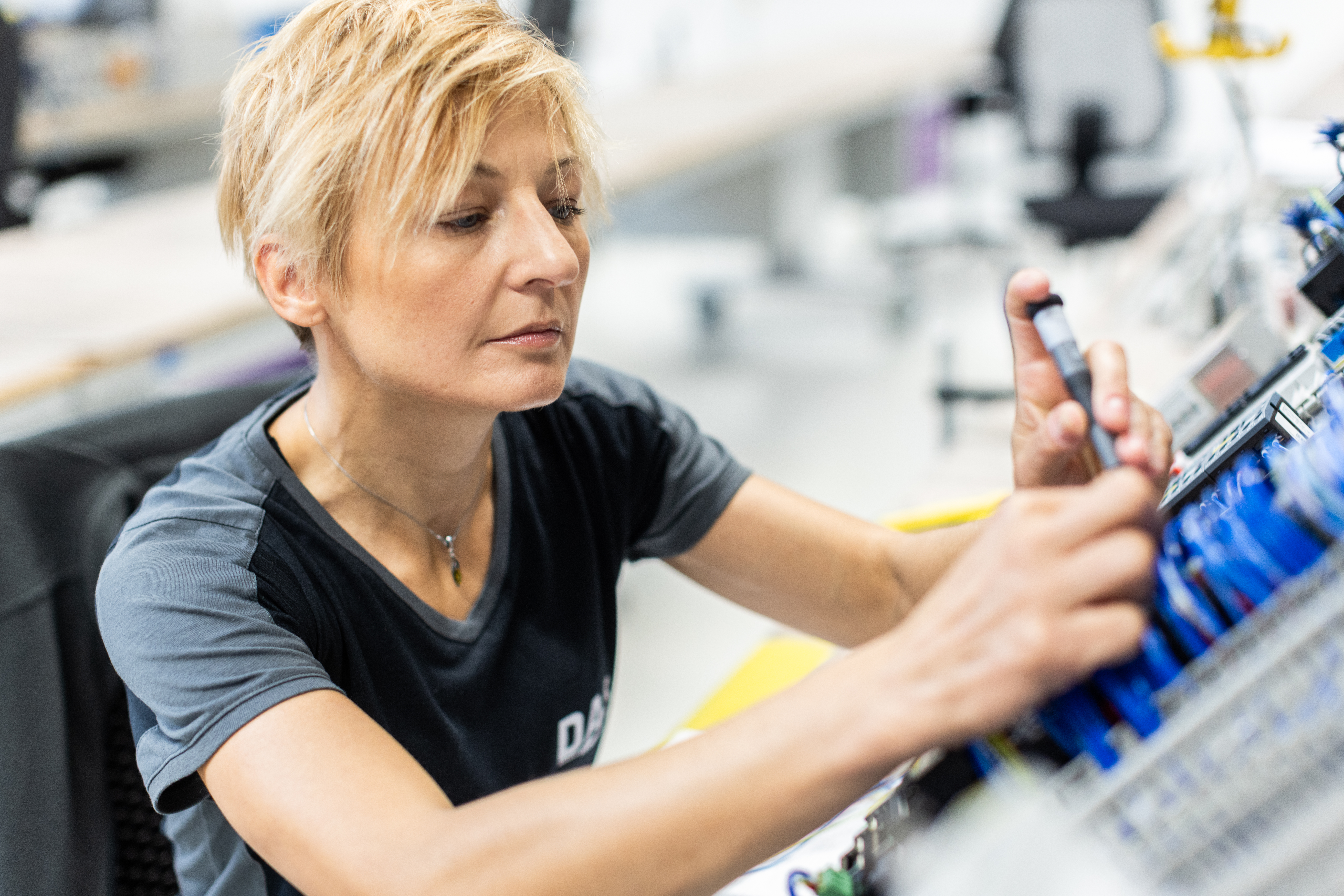 An individual with short blond hair is focused on handling electronic components in a modern laboratory setting.
