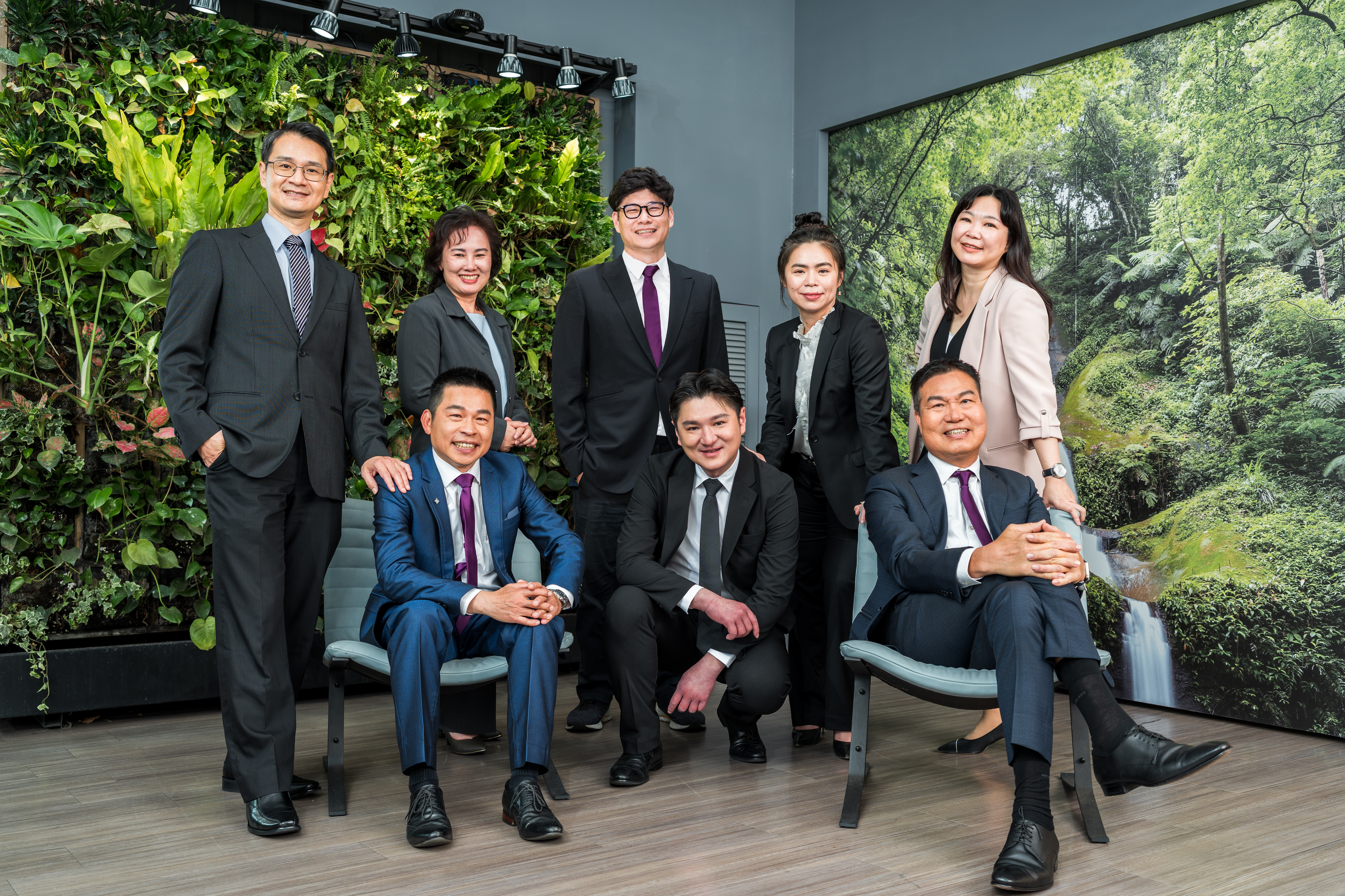 一組穿著正式商務服裝的人們在室內植物牆前微笑合影，背景是綠色的植物景觀。
