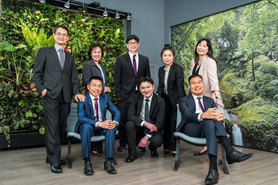 台灣管理團隊 一組穿著正式商務服裝的人們在室內植物牆前微笑合影,背景是綠色的植物景觀。