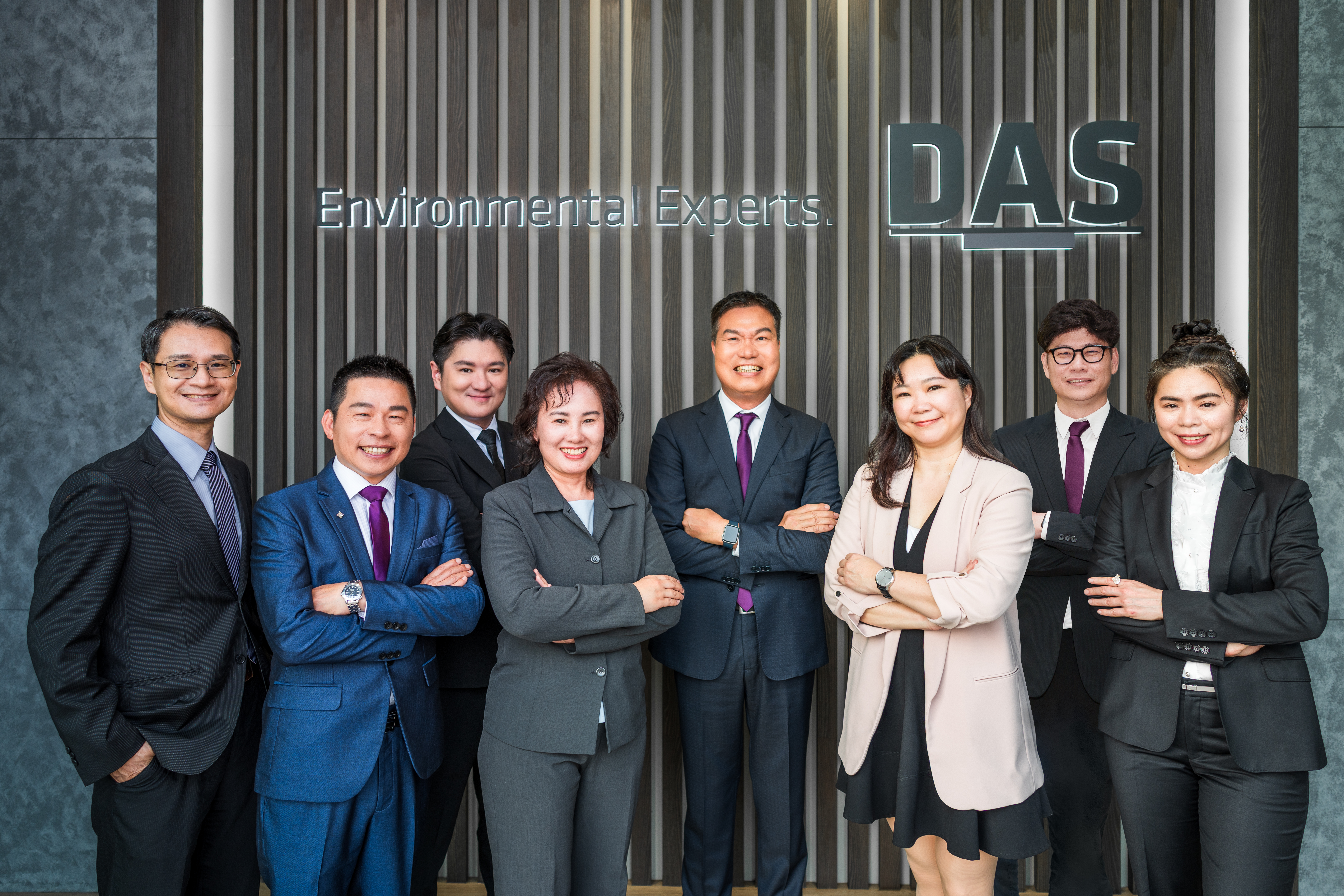 這張圖片展示了一群穿著正裝的專業人士，站在DAS標誌前，背景是刻有「Environmental Experts」字樣的牆壁，他們全都面帶微笑並自信地交叉雙臂。