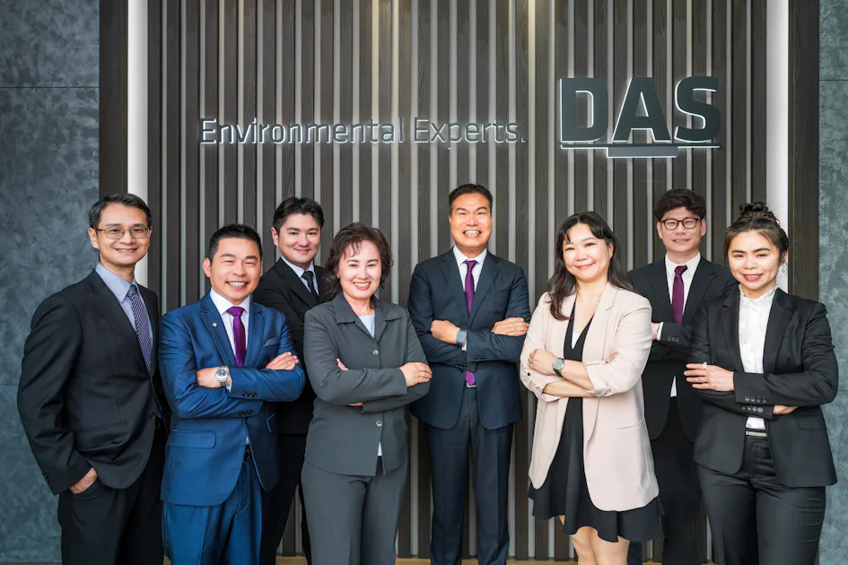 DAS TW 主管群 這張圖片展示了一群穿著正裝的專業人士,站在DAS標誌前,背景是刻有「Environmental Experts」字樣的牆壁,他們全都面帶微笑並自信地交叉雙臂。