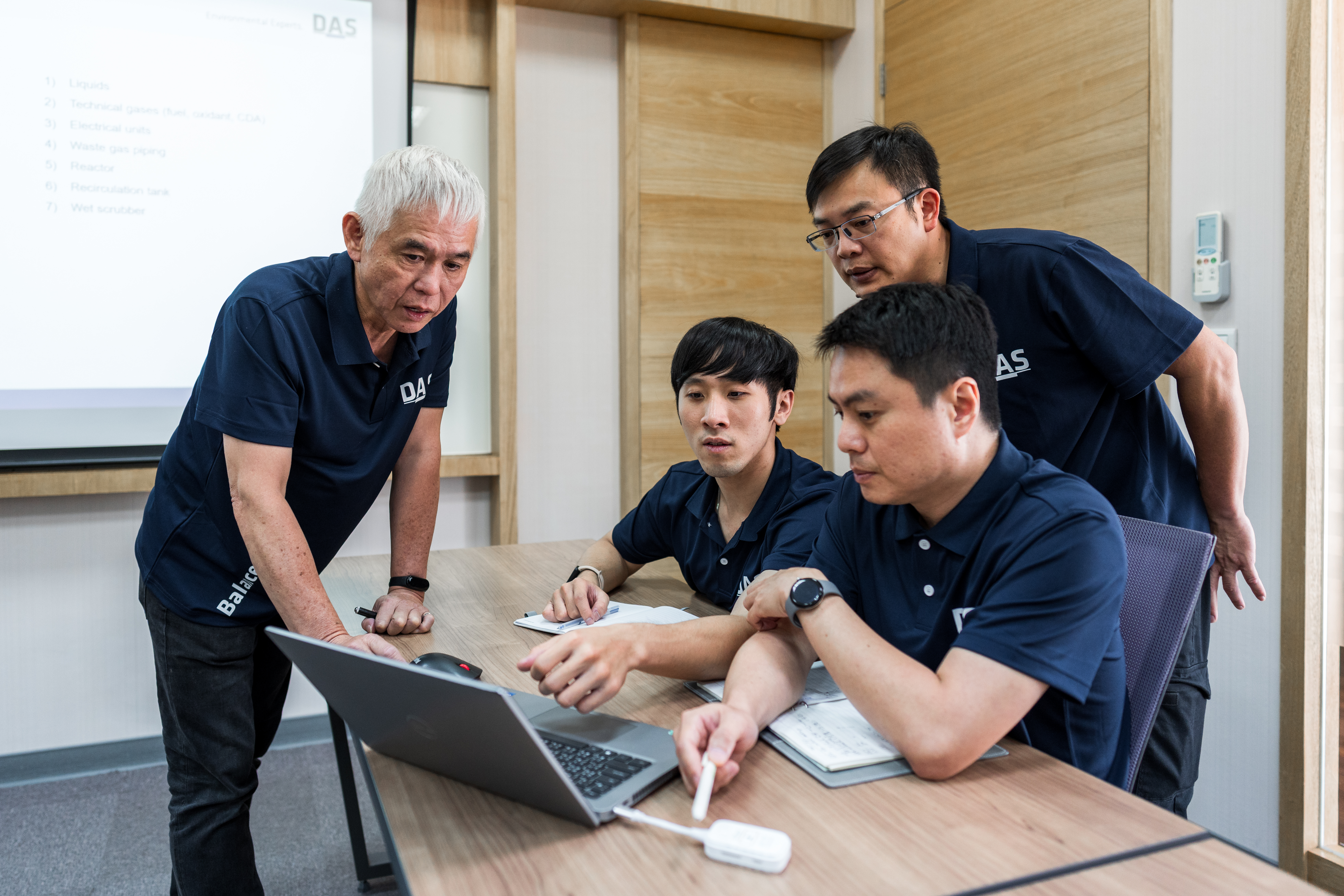 不確定有關SEO關鍵字是否為不適當關鍵字。一位年長男子和三位中年男子正在一間現代化會議室中集中討論，圍繞在一張放有筆記型電腦的木製桌子旁，專注地查看屏幕。