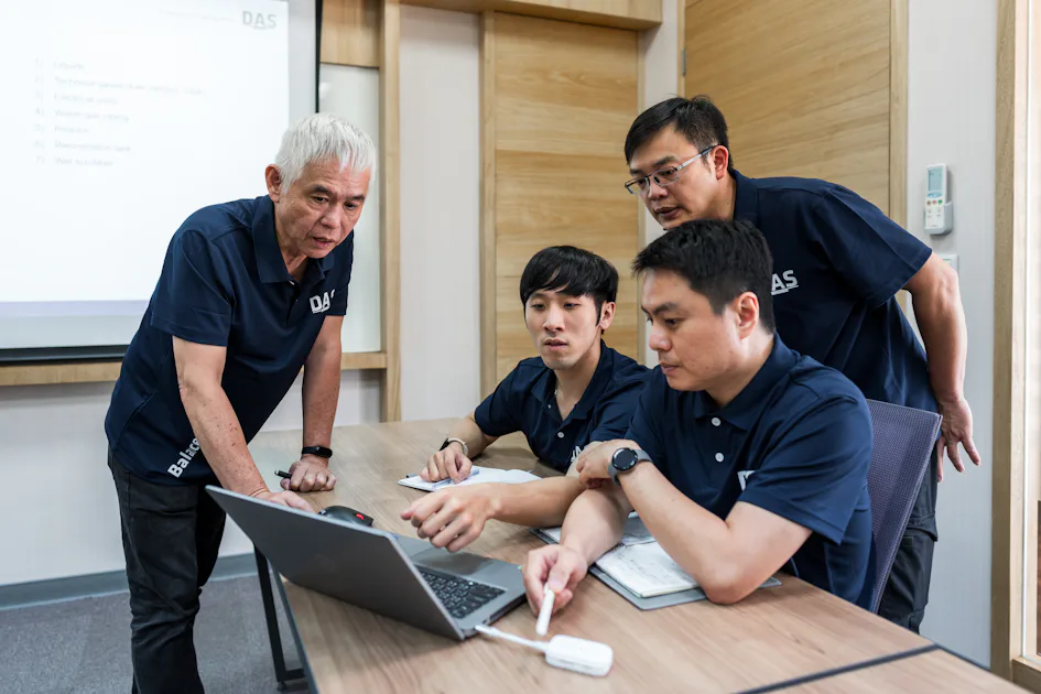 case study 不確定有關SEO關鍵字是否為不適當關鍵字。一位年長男子和三位中年男子正在一間現代化會議室中集中討論,圍繞在一張放有筆記型電腦的木製桌子旁,專注地查看屏幕。