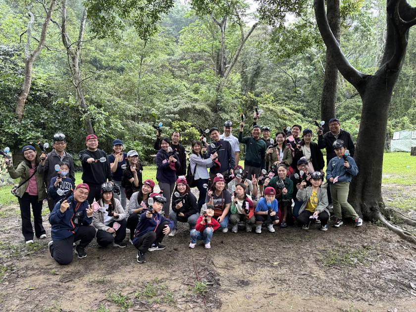 漆彈 一群人在樹林中的戶外郊遊活動合影,他們站在樹下,身穿休閒服裝,展現出開心的表情。