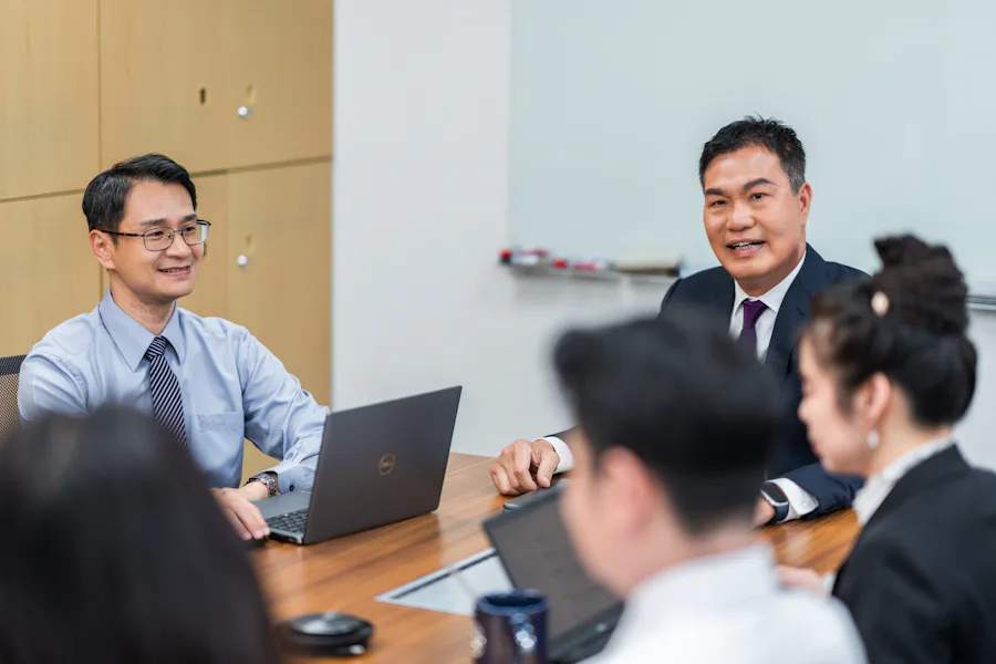 工作 一群商務人士在會議室進行討論,桌上有兩台打開的筆記型電腦,旁邊是白板和資料夾,代表商業會議的專業環境。